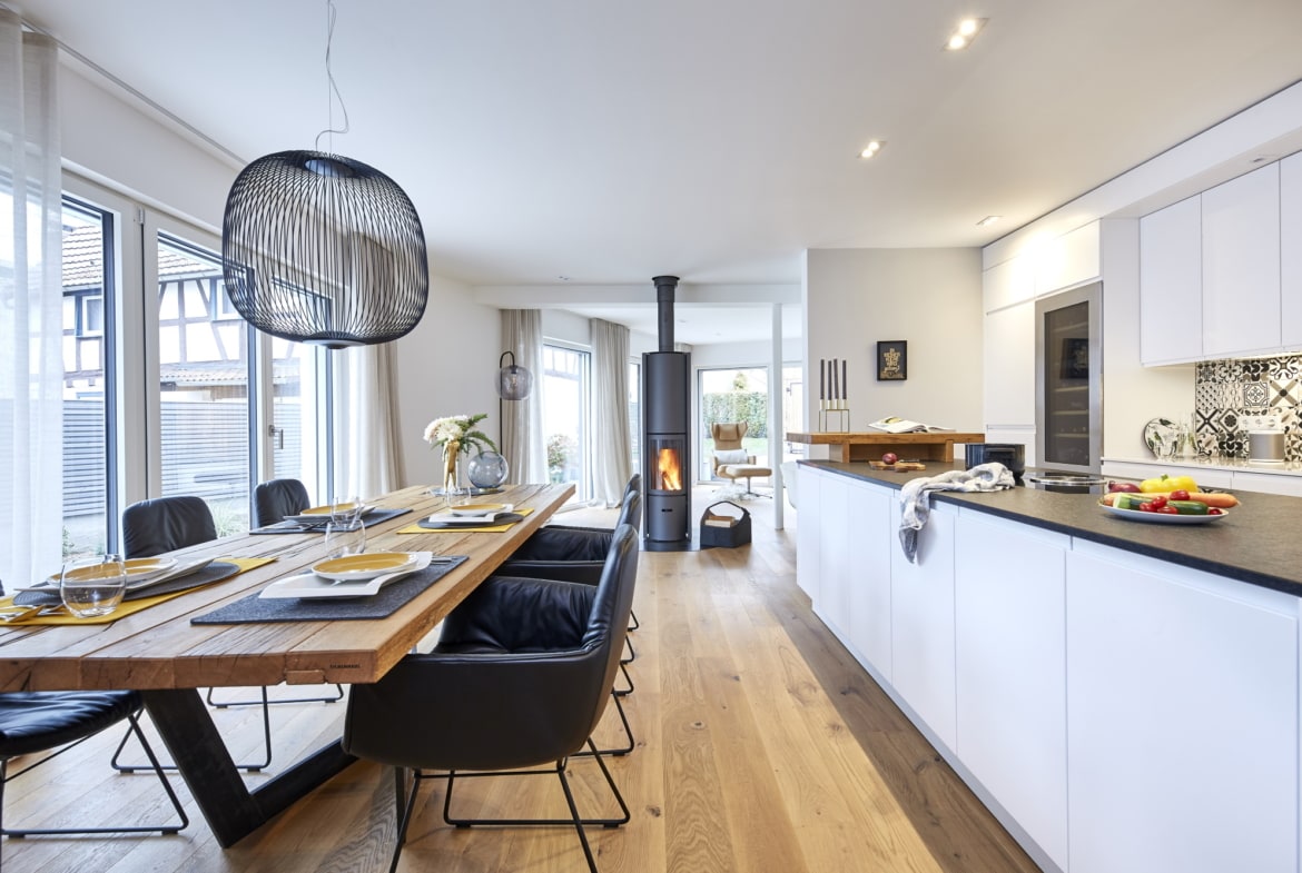 Offene Küche modern weiß mit großem Esstisch rustikal aus Holz & Kaminofen als Raumteiler - Ideen Inneneinrichtung Haus Design Baufritz STADTHAUS EHRMANN - HausbauDirekt.de